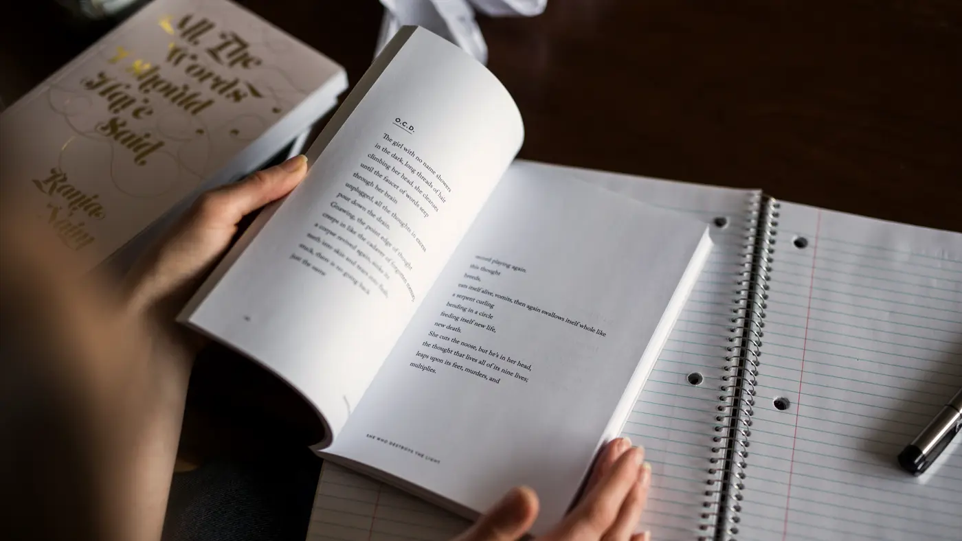 Hands holding an open book beside a notebook