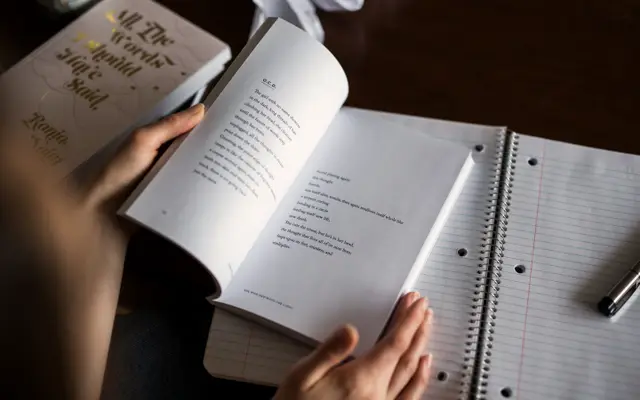 Hands holding an open book beside a notebook