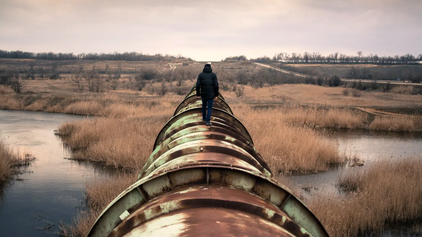 Person walking along the top of a large pipeline across a marsh