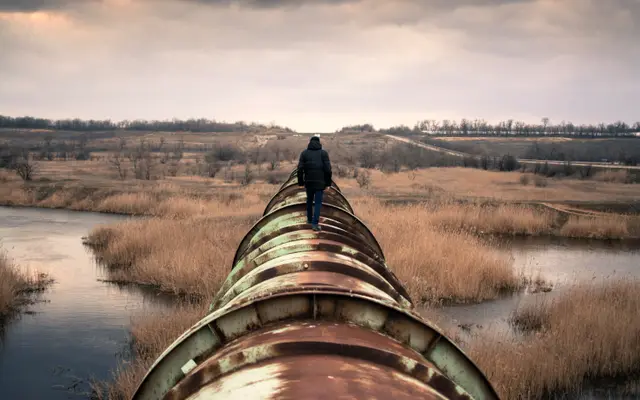 Person walking along the top of a large pipeline across a marsh