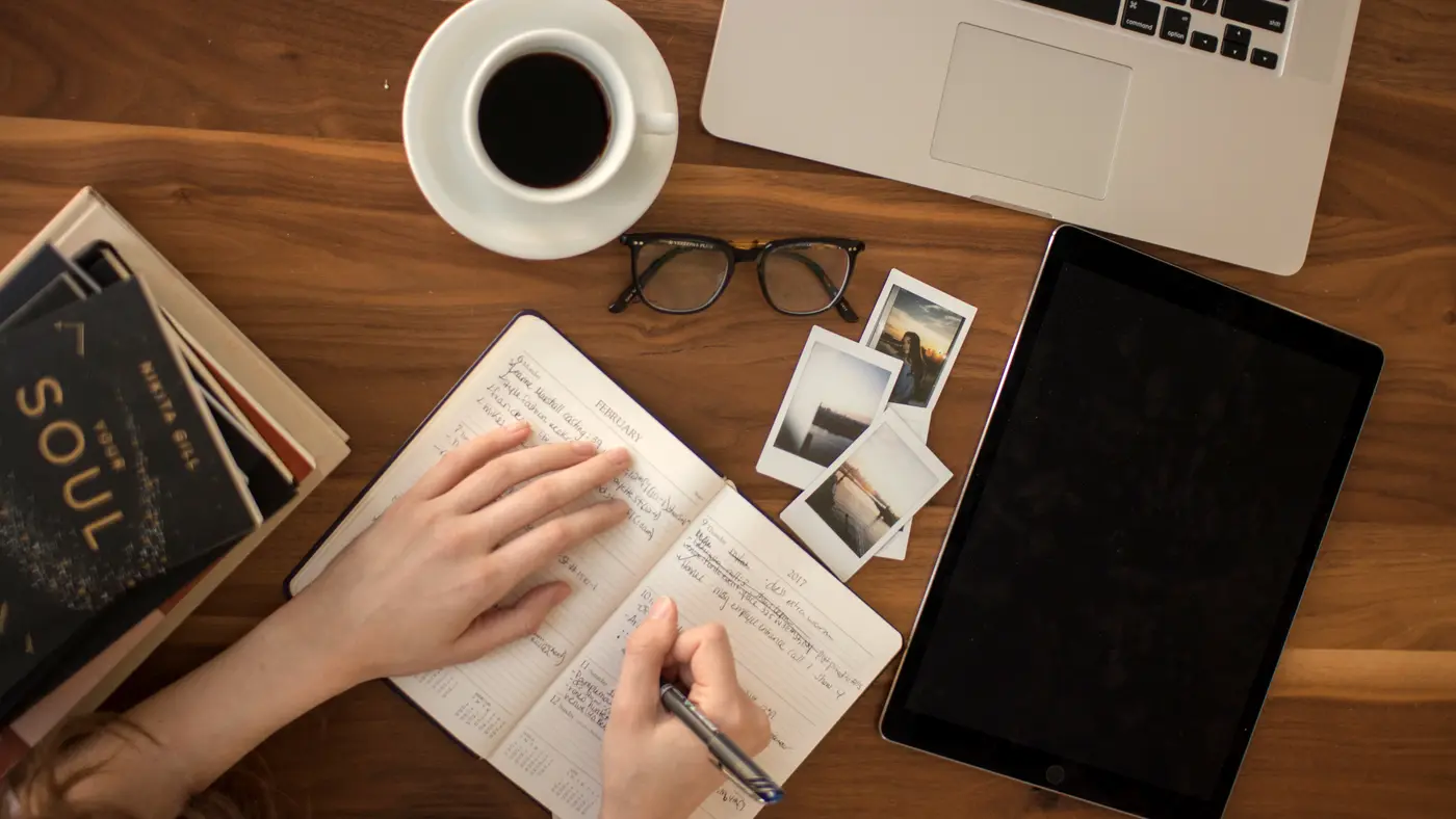 Overhead view of a hand writing in a notebook beside a laptop and coffee