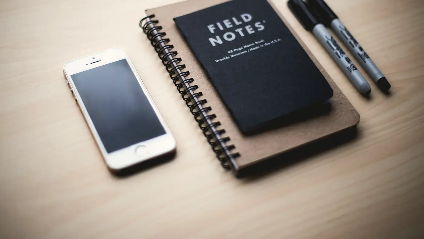 Field notebook, pens and a phone arranged on a desk