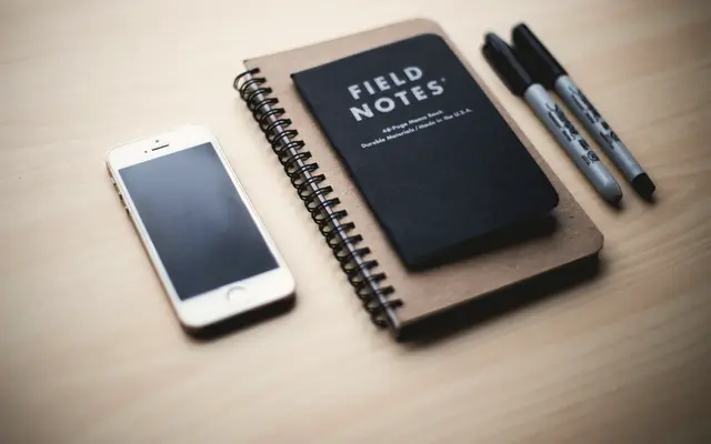 Field notebook, pens and a phone arranged on a desk