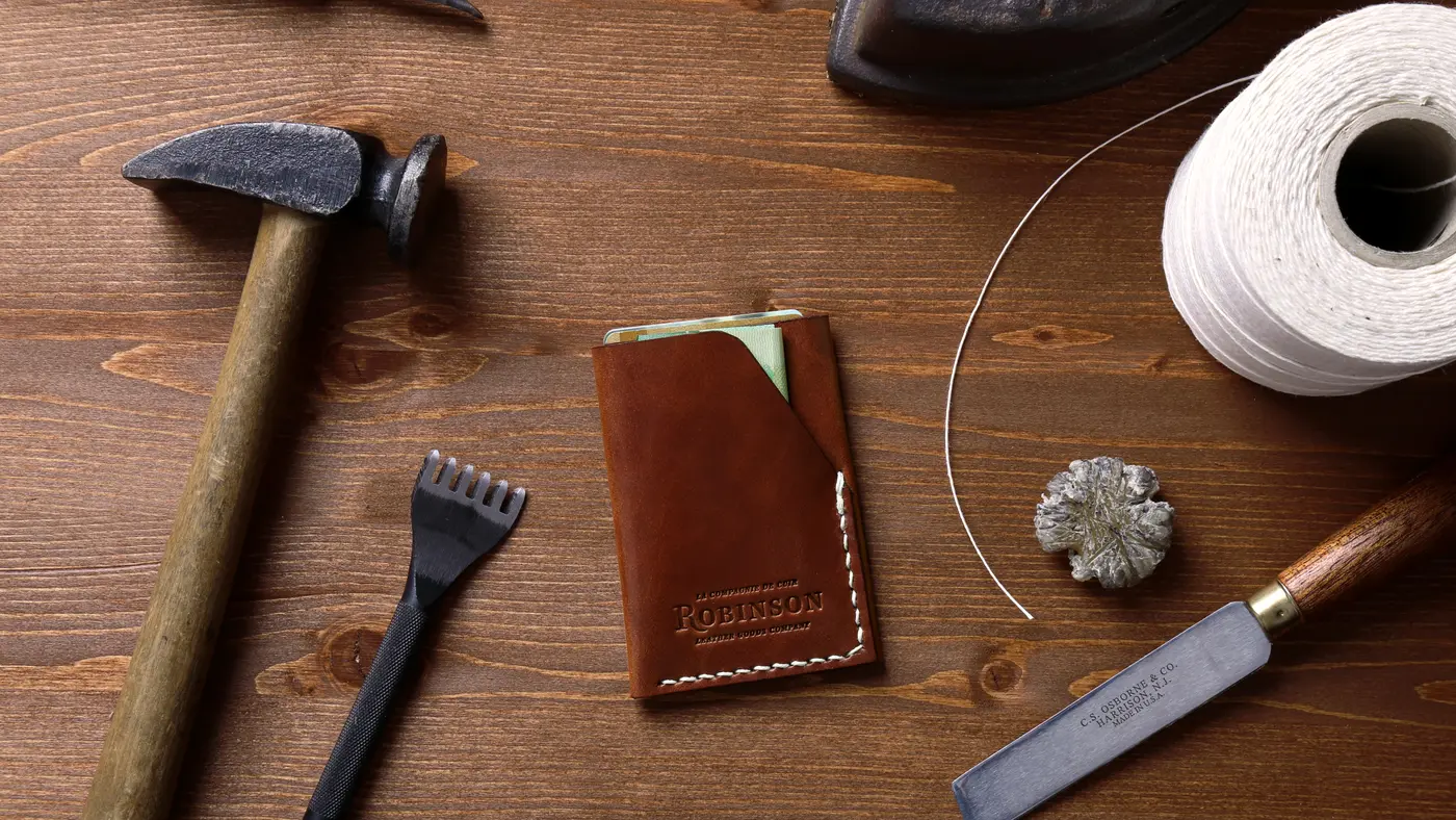 Hammer, leather wallet, chisel and thread laid out on a wooden workbench