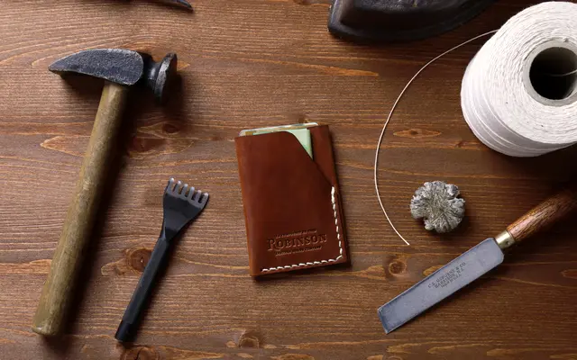 Hammer, leather wallet, chisel and thread laid out on a wooden workbench