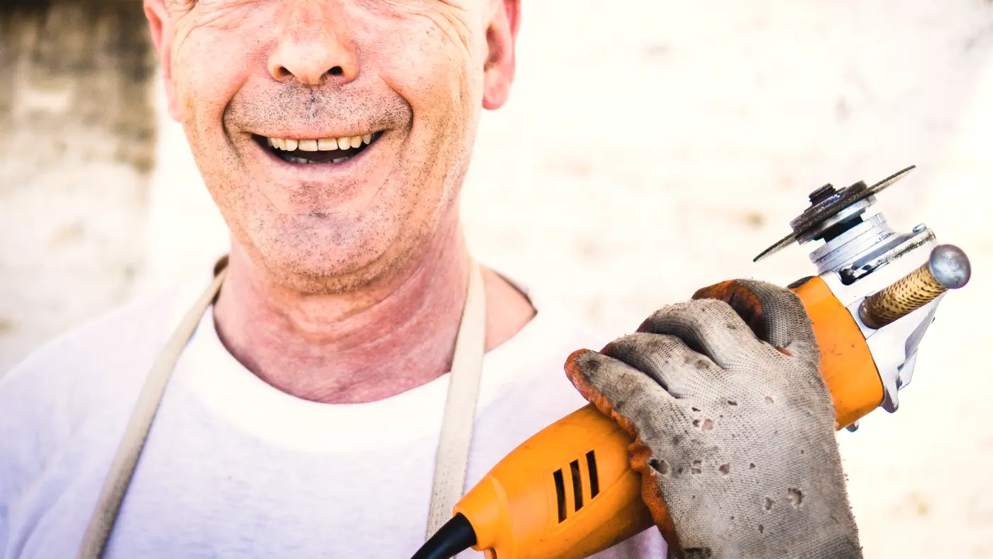 Smiling worker in an apron holding a power tool