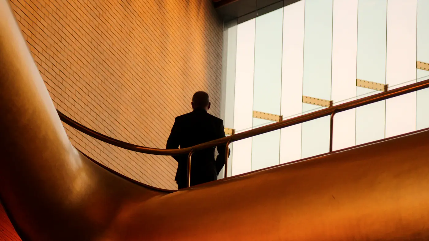 Man walking down a curved staircase beside tall windows