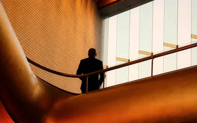 Man walking down a curved staircase beside tall windows