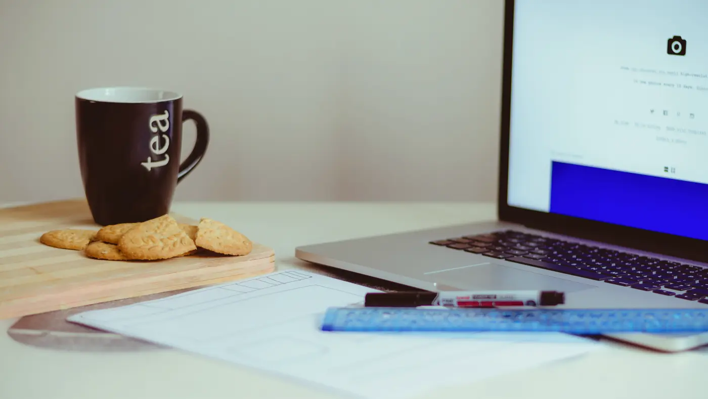 Desk with a laptop, printed documents, a ruler, pens and a mug of tea