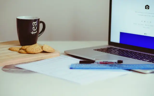 Desk with a laptop, printed documents, a ruler, pens and a mug of tea