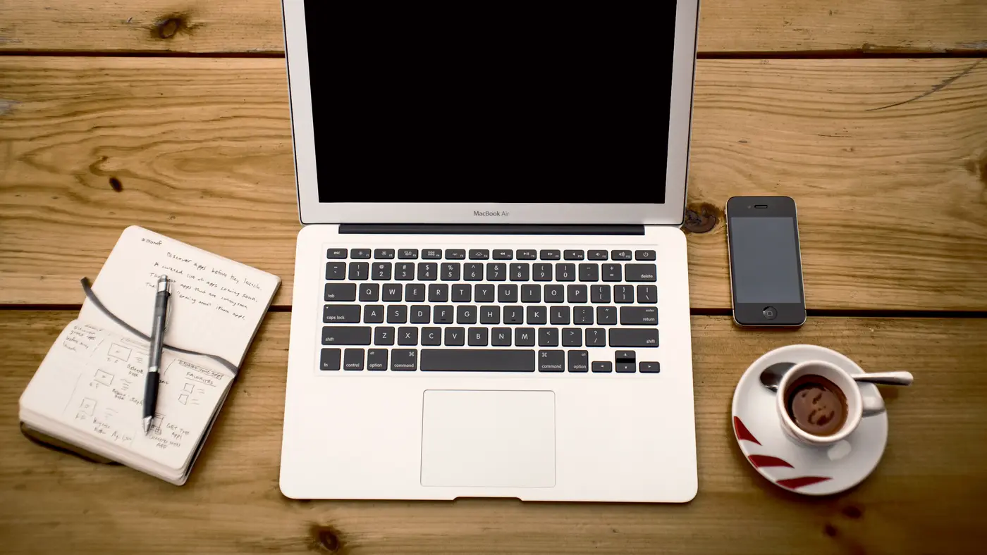 Laptop, notebook, pen, phone and coffee on a wooden desk