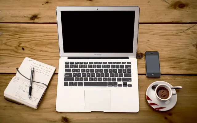 Laptop, notebook, pen, phone and coffee on a wooden desk