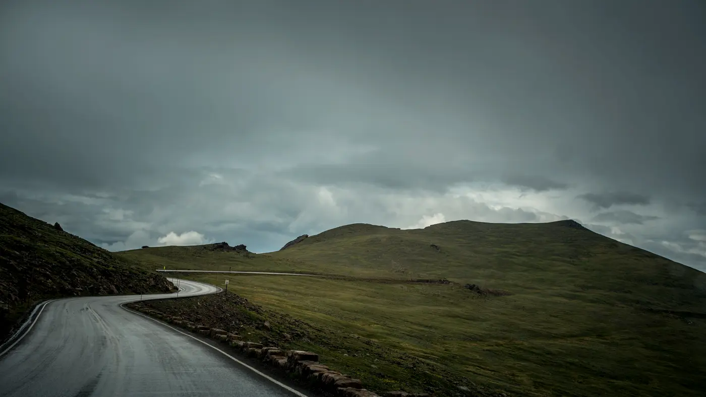 Empty road winding across hills under dark storm clouds