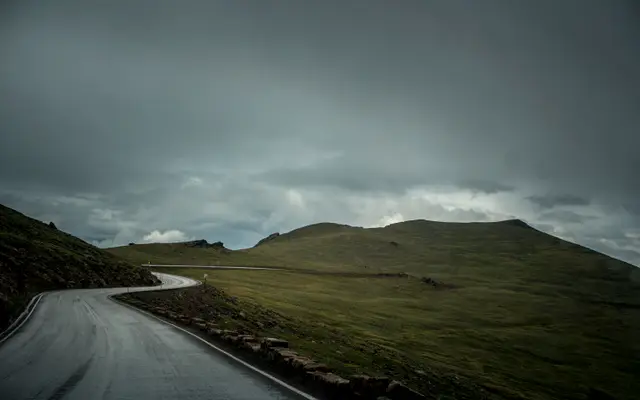 Empty road winding across hills under dark storm clouds