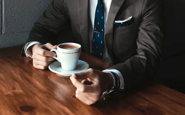 Businessman in a suit with a cup of coffee at a wooden table