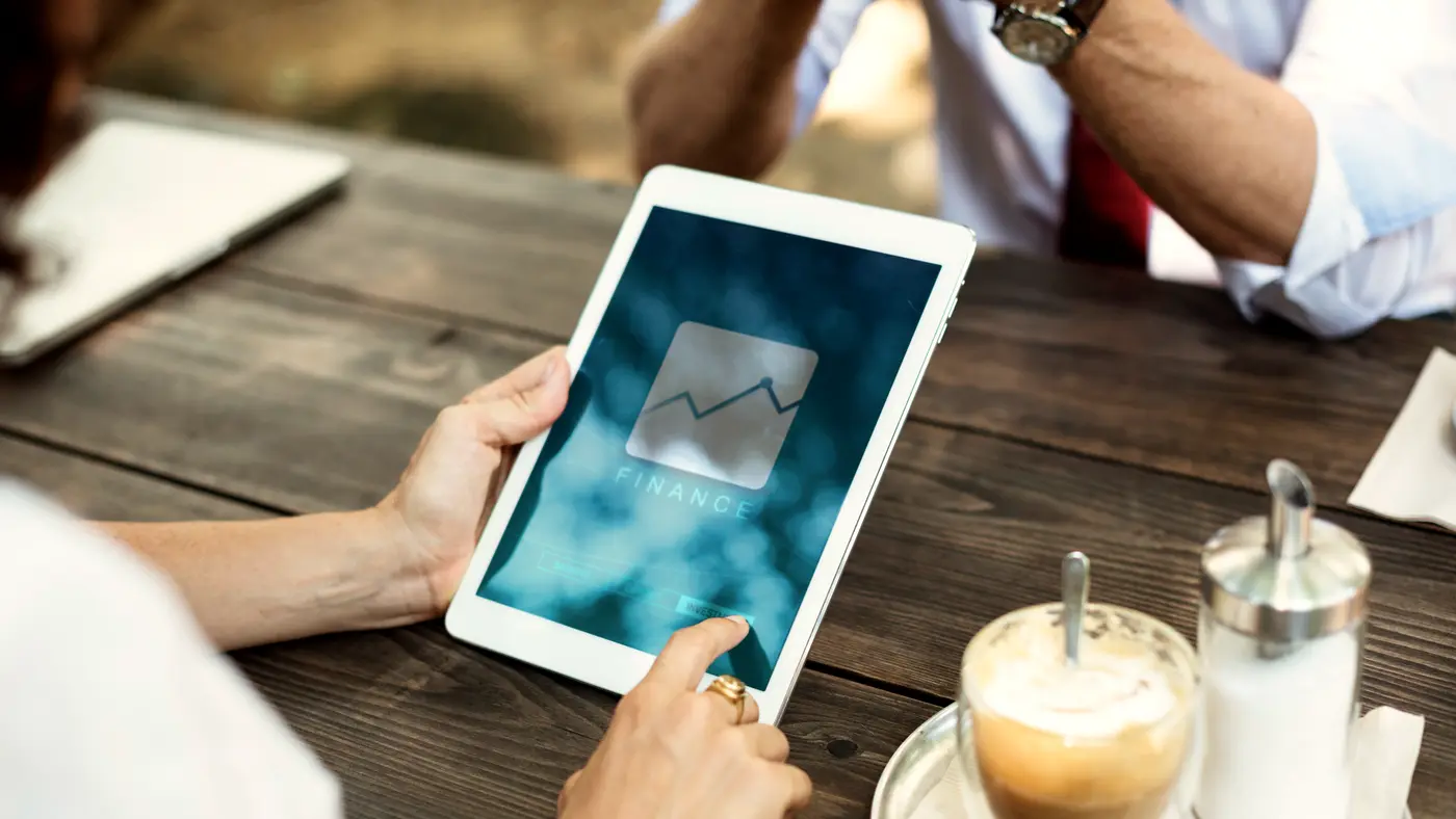 Hands holding a tablet showing a growth chart next to a cup of coffee