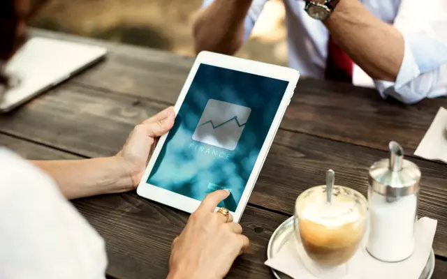 Hands holding a tablet showing a growth chart next to a cup of coffee