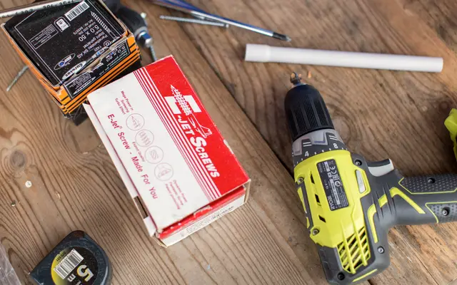 Cordless drill, tape measure and a box of fasteners on a wooden workbench