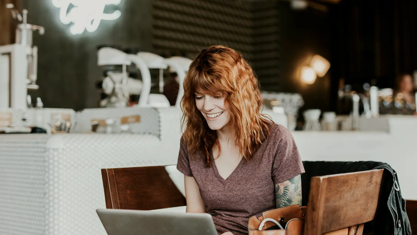 Woman smiling at her laptop in a coffee shop