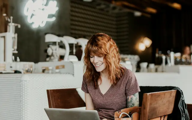Woman smiling at her laptop in a coffee shop