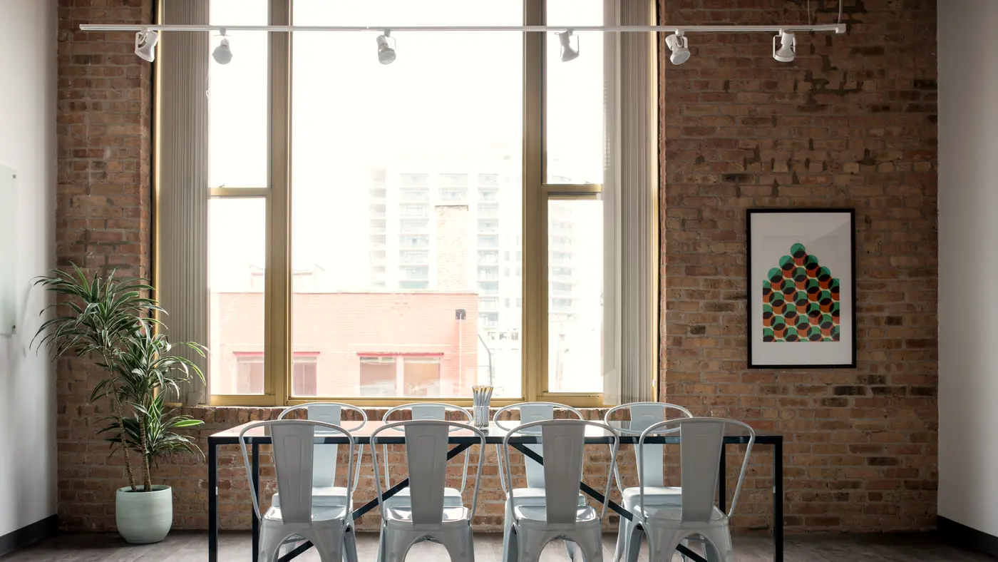 Conference table and chairs in a brick-walled meeting room with city windows