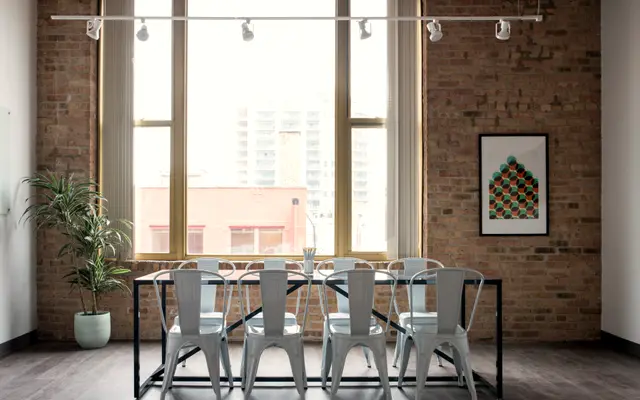 Conference table and chairs in a brick-walled meeting room with city windows