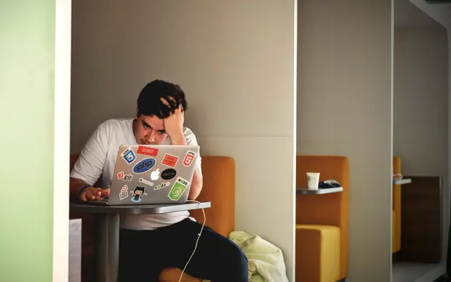 Man holding his head in frustration while working on a laptop