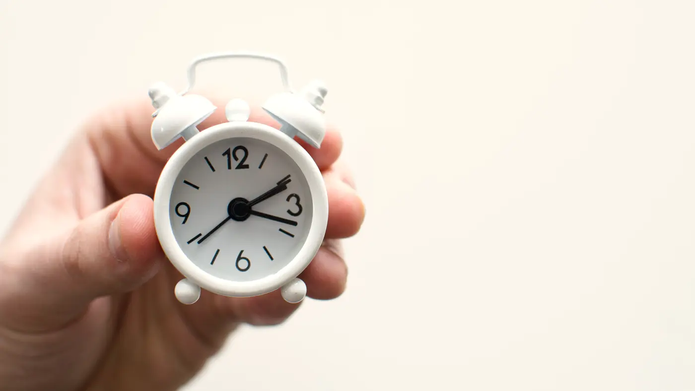 Hand holding a small white alarm clock