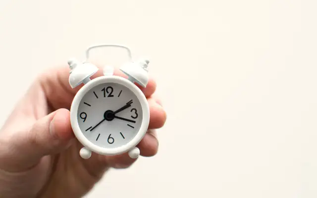 Hand holding a small white alarm clock