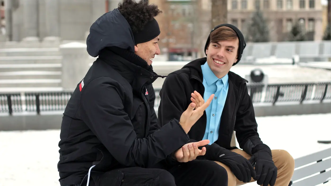 Two men talking on a bench outdoors in winter