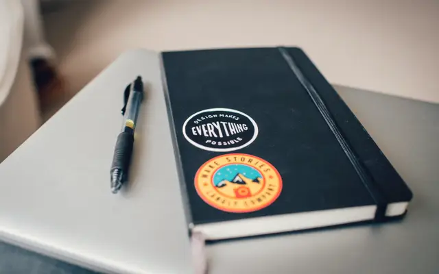 Black notebook and pen resting on a laptop