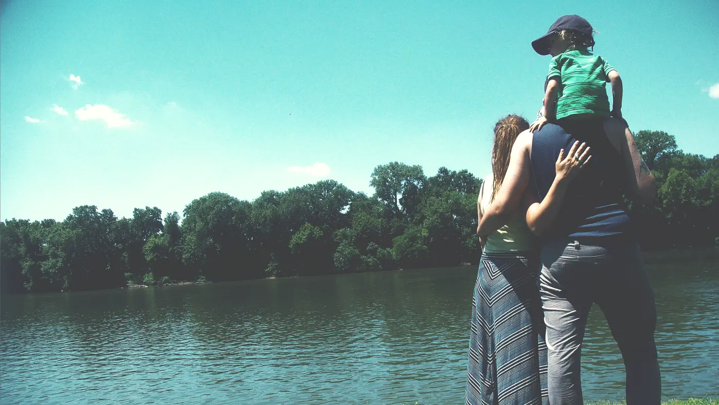 Father carrying a child on his shoulders beside a lake