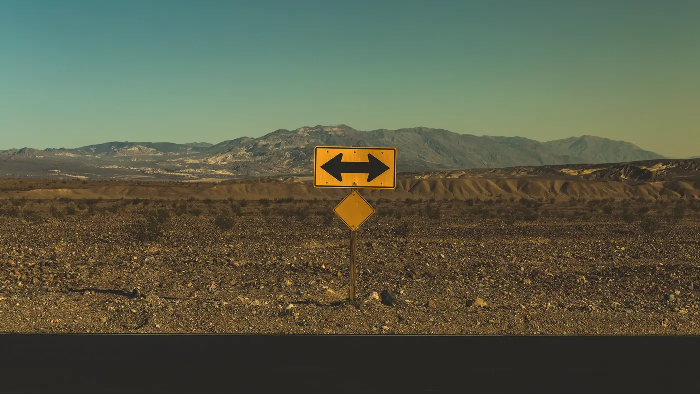 Two-way arrow road sign standing alone in a desert valley