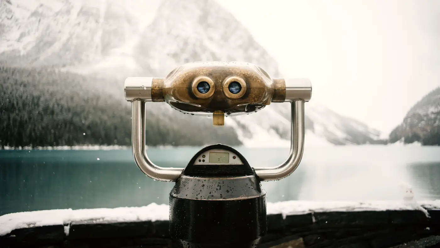 Coin-operated binoculars overlooking a lake and snowy mountains