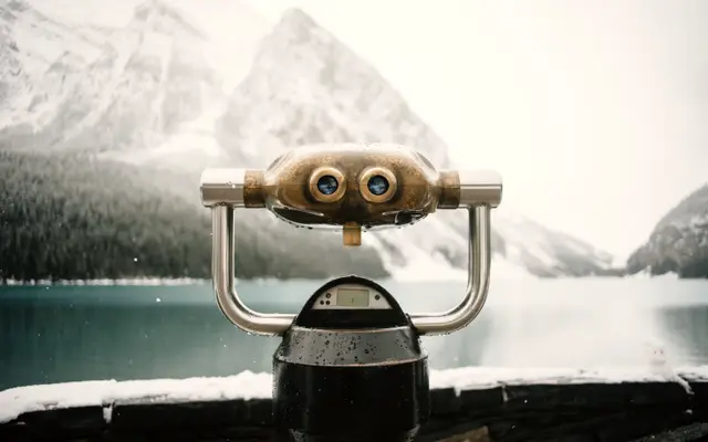 Coin-operated binoculars overlooking a lake and snowy mountains