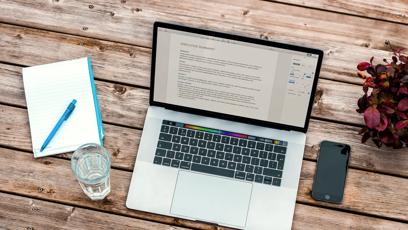 Overhead view of a laptop showing a document next to a notepad and pen