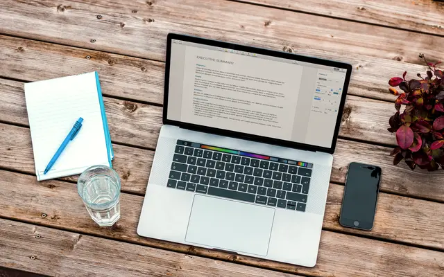 Overhead view of a laptop showing a document next to a notepad and pen